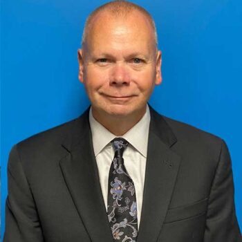 a man in a suit and tie standing next to a blue wall
