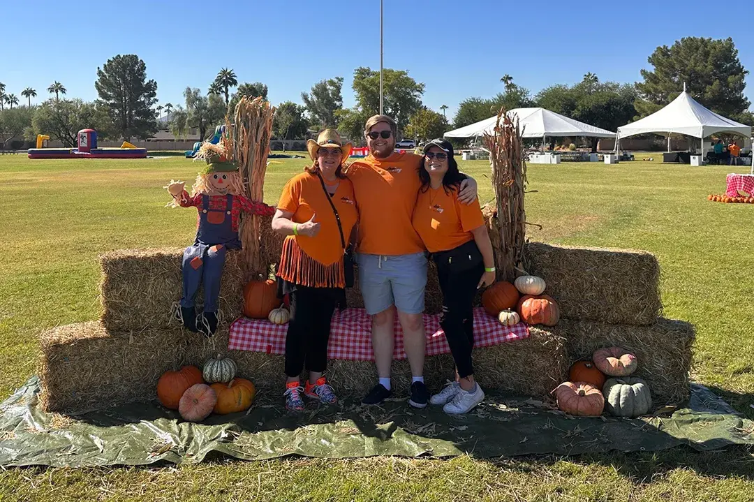 People posing in front of hay stack and pumpkins